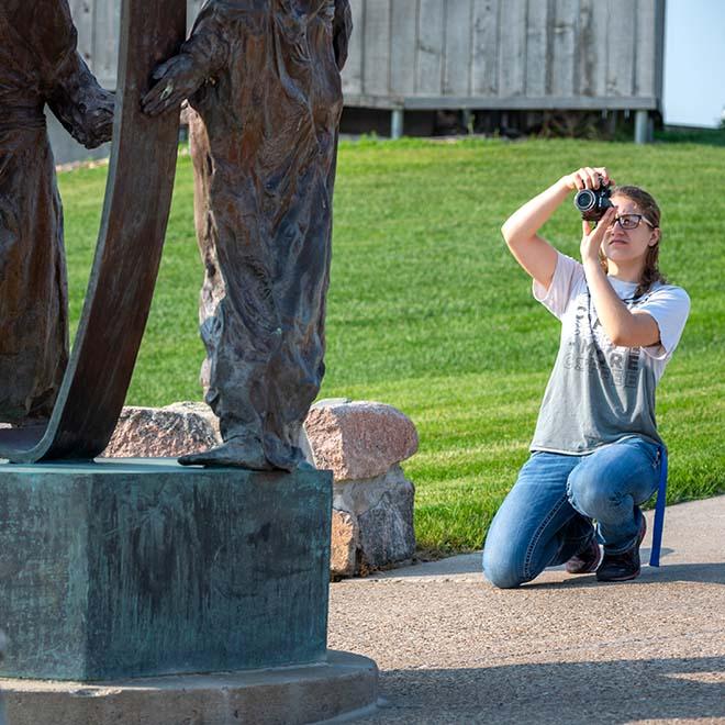 Female photography student taking photo of statue on campus