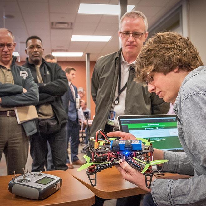 Engineering student showing his invention to three leaders.