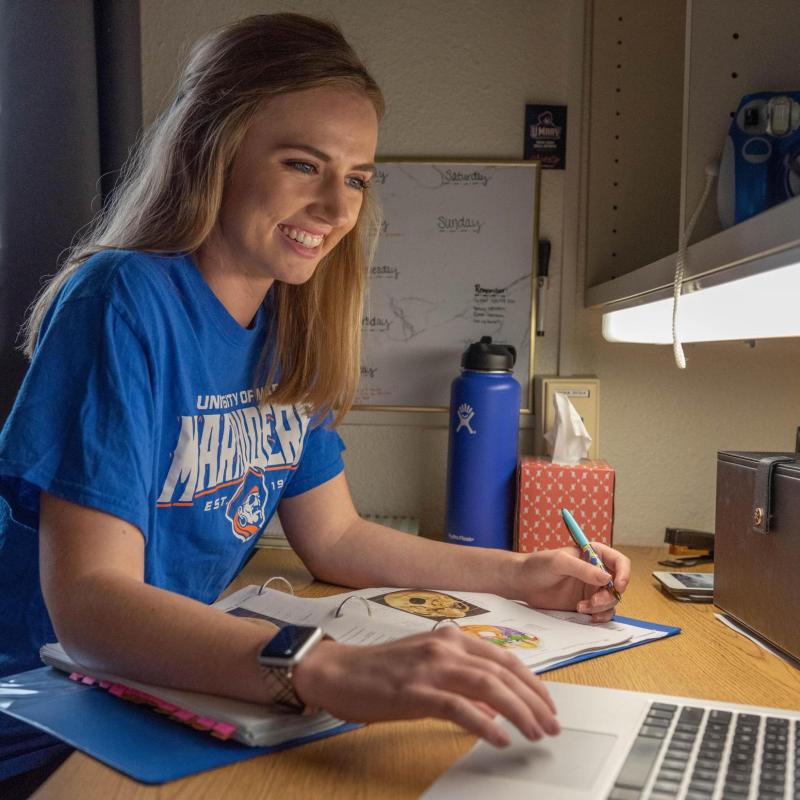 Female student typing on laptop in her residence hall.