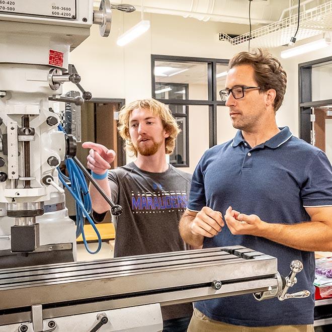 Engineering student pointing at machinery and asking professor a question