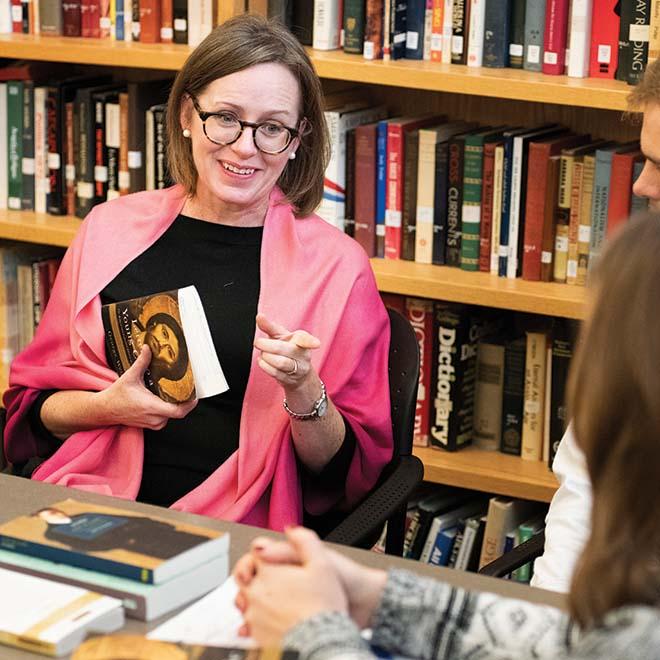 Three students sitting at a table with a professor discussing a religious book