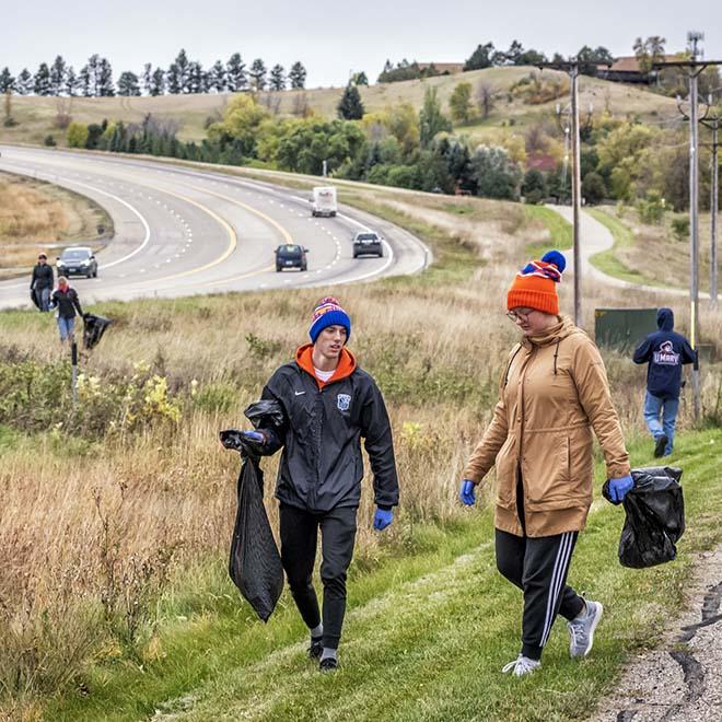 Two Mary students carrying trash bags alongside the highway