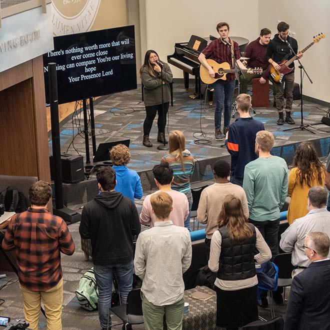 Large group of students gathered for worship with four musicians on stage 