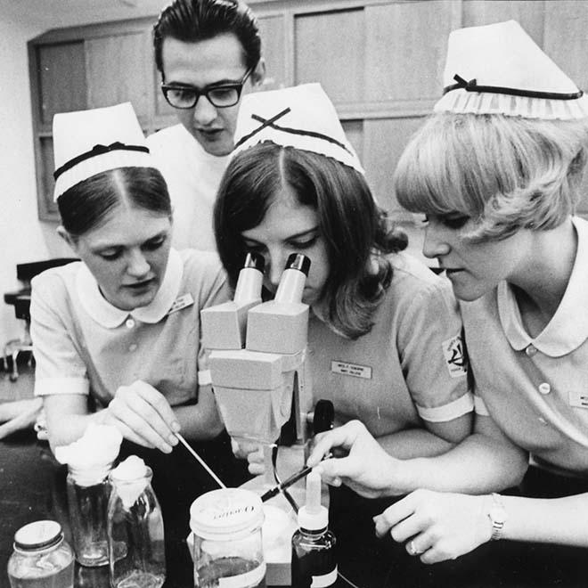 One Nursing student looking in microscope with three other nursing students around her in 1960.