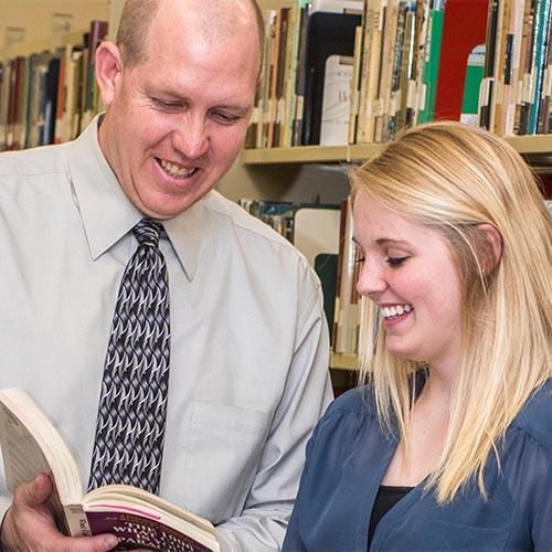 Career advisor showing a female student a book in the library.