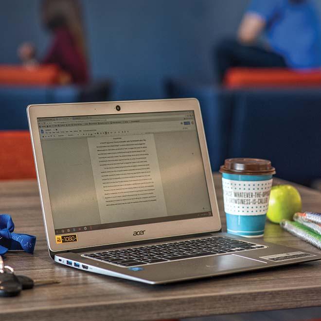 Laptop on table with coffee, apple, and notebooks