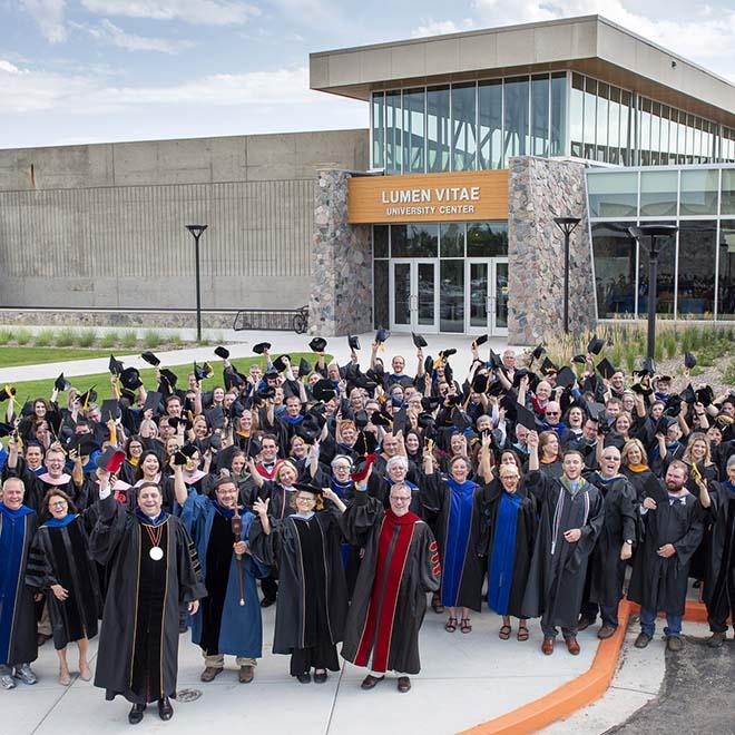 Large group of faculty in their regalia waving outside campus center