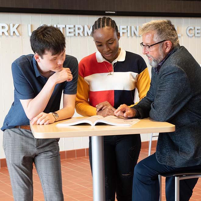 Professor and two business students looking at textbook