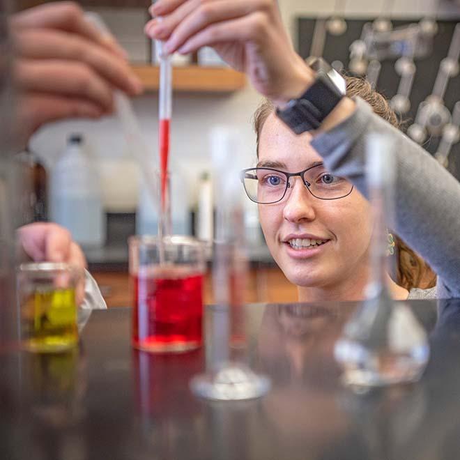 Female student dropping red liquid into beaker