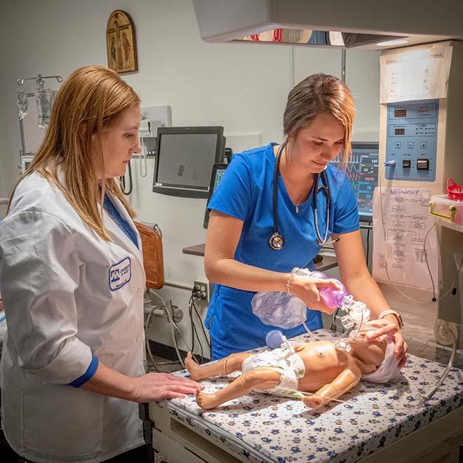 Student nurse giving oxygen to a mannequin of a baby in simulation lab with professor monitoring
