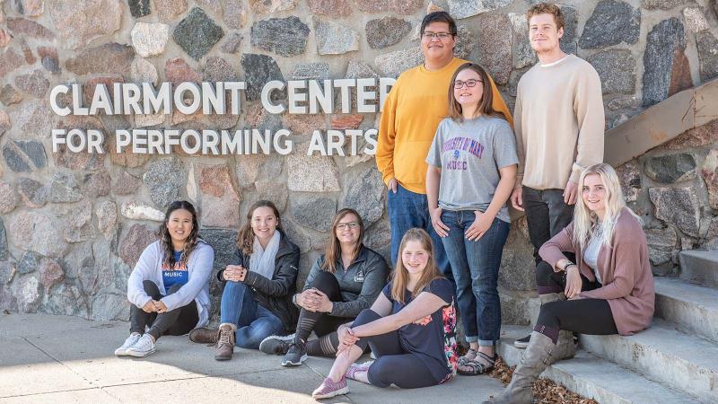 Group of smiling students by the Clairmont for Performing Arts signage on the exterior of the building