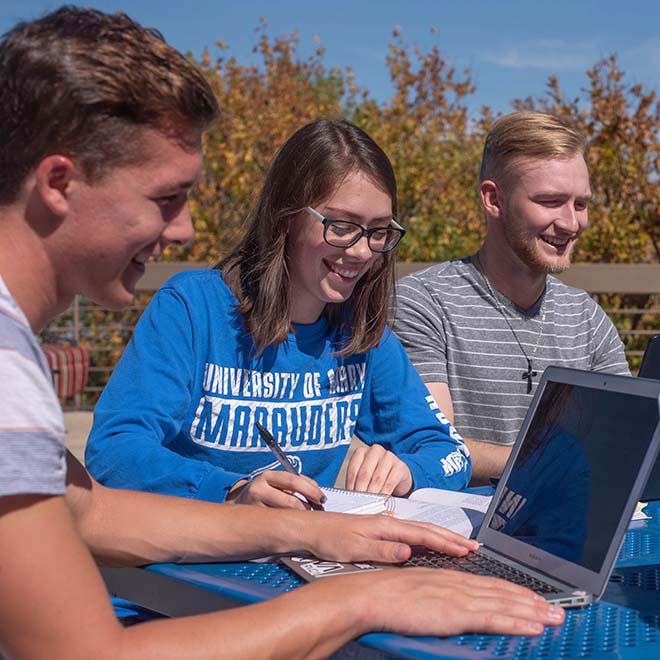Three students studying together outside at table
