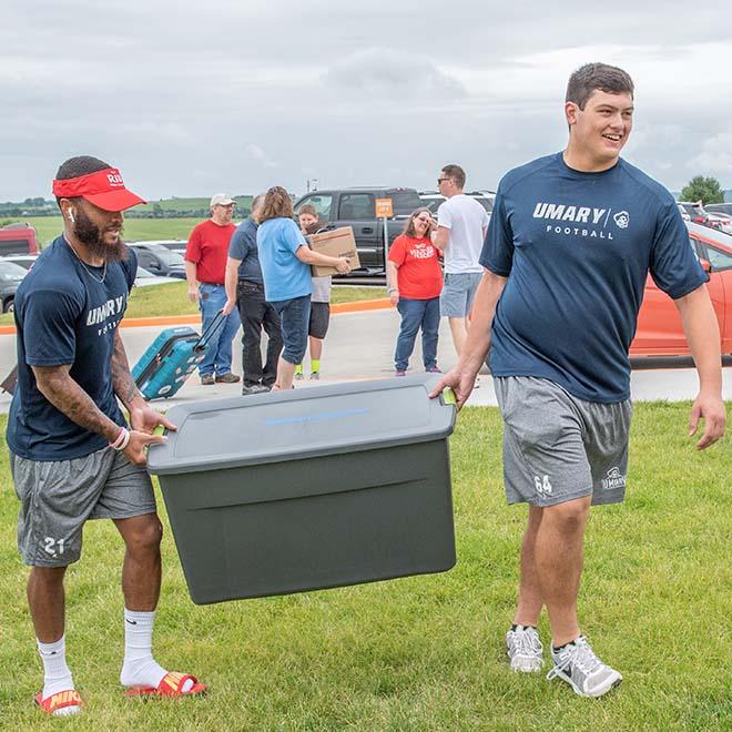 University of Mary football players carrying a tote for new students on campus.