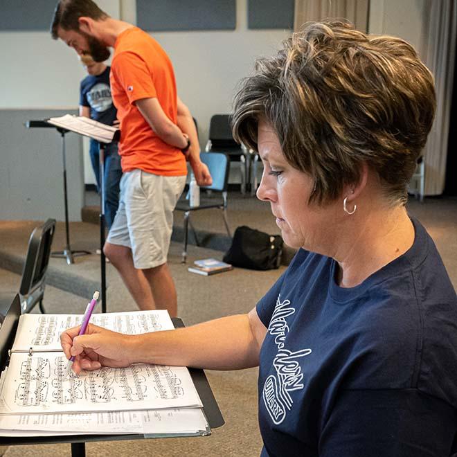 Adult music student taking notes on sheet music with two students in the background