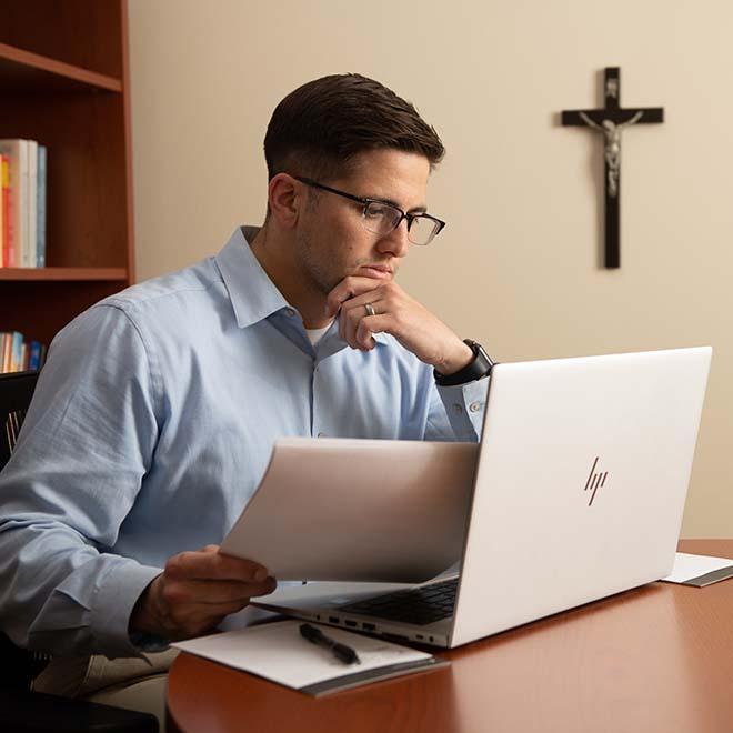 Young professional working on laptop with crucifix in background