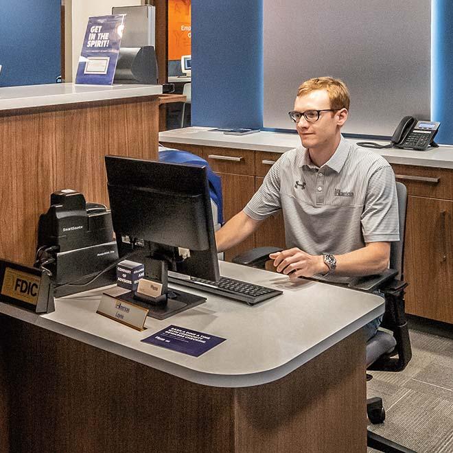 Business student at desk working on computer at the on campus bank