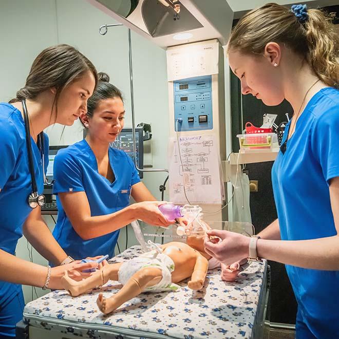 Three nursing students giving breathing treatment to baby mannequin