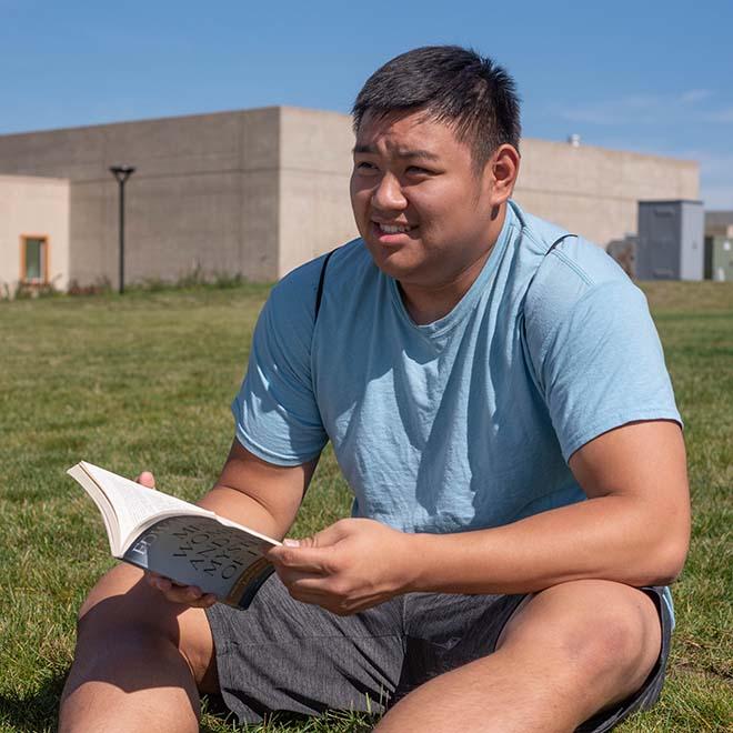 Male year-round campus student studying outside on a summer day