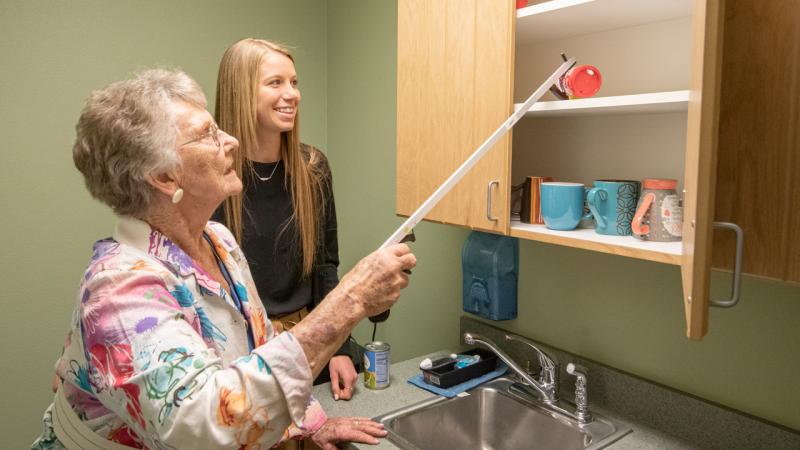 Student showing elderly woman how to get a cup with her arm extender