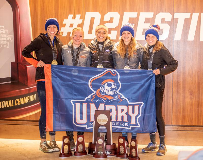 Students holding the UMary Athletics flag with their trophies