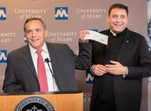 ETP’s Chris Curia holds up check donation before presenting to University of Mary President Monsignor Shea