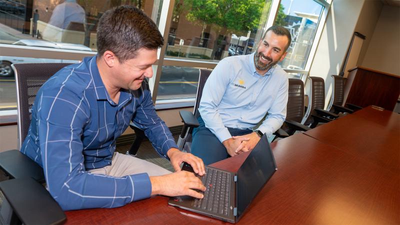 Brennan Quintus working with an employee at the table with a view of the town out the window