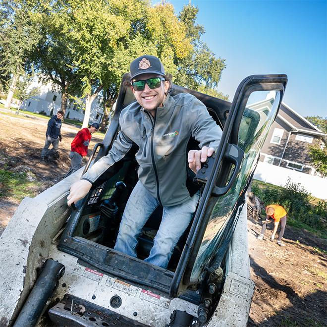 student driving a bobcat during day of service