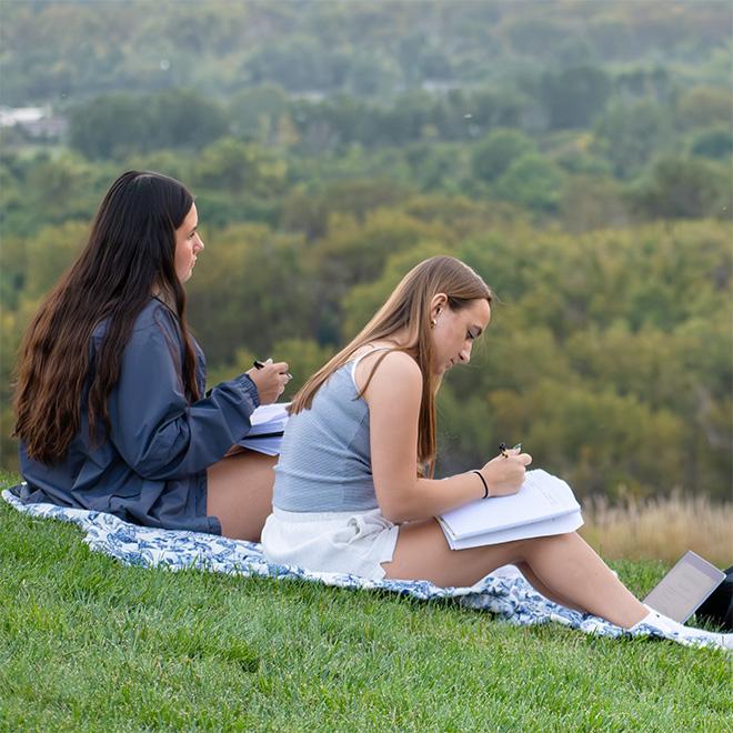 students studying outside on the shire with the view in the background of the river and trees
