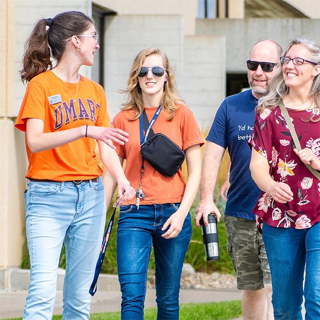 A student in orange walking around campus getting a tour from an admission rep