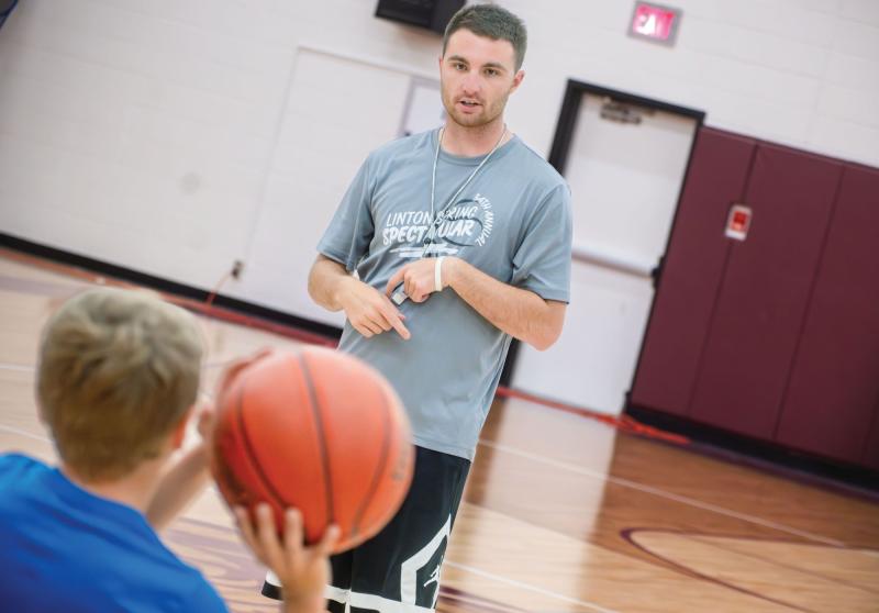 Physical education teacher Alex Scherr coaches a student on shooting a basketball.