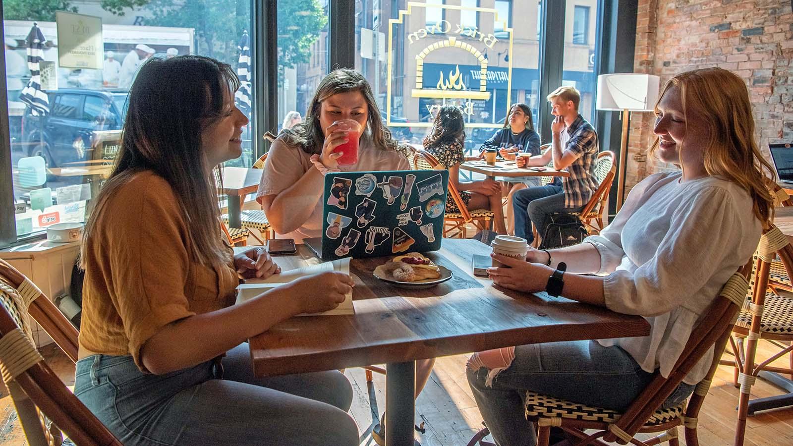 Three female students enjoying coffee and pastries at Brick Oven Bakery in downtown Bismarck