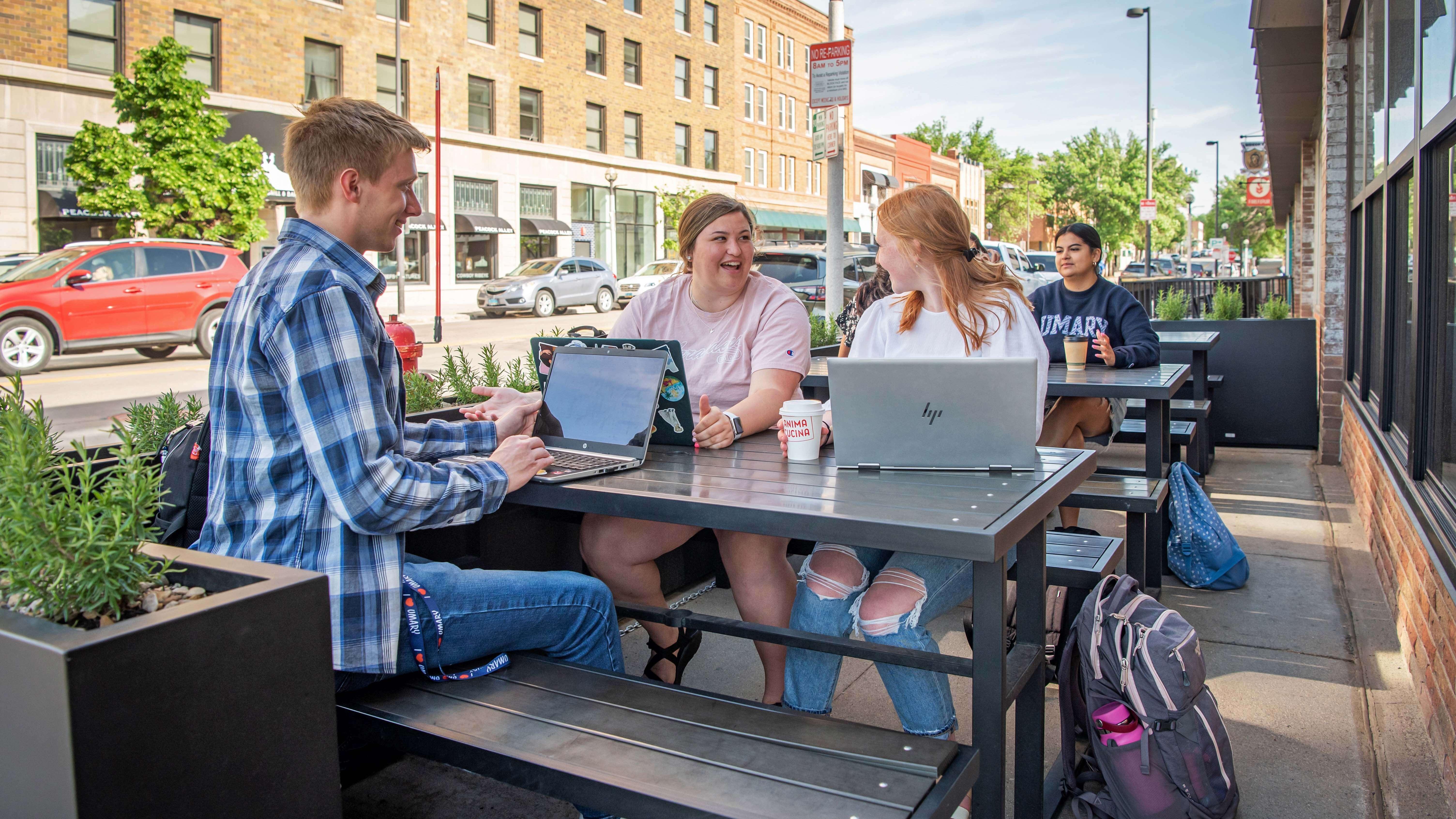 Three University of Mary students sitting at picnic table outside a restaurant in downtown Bismarck