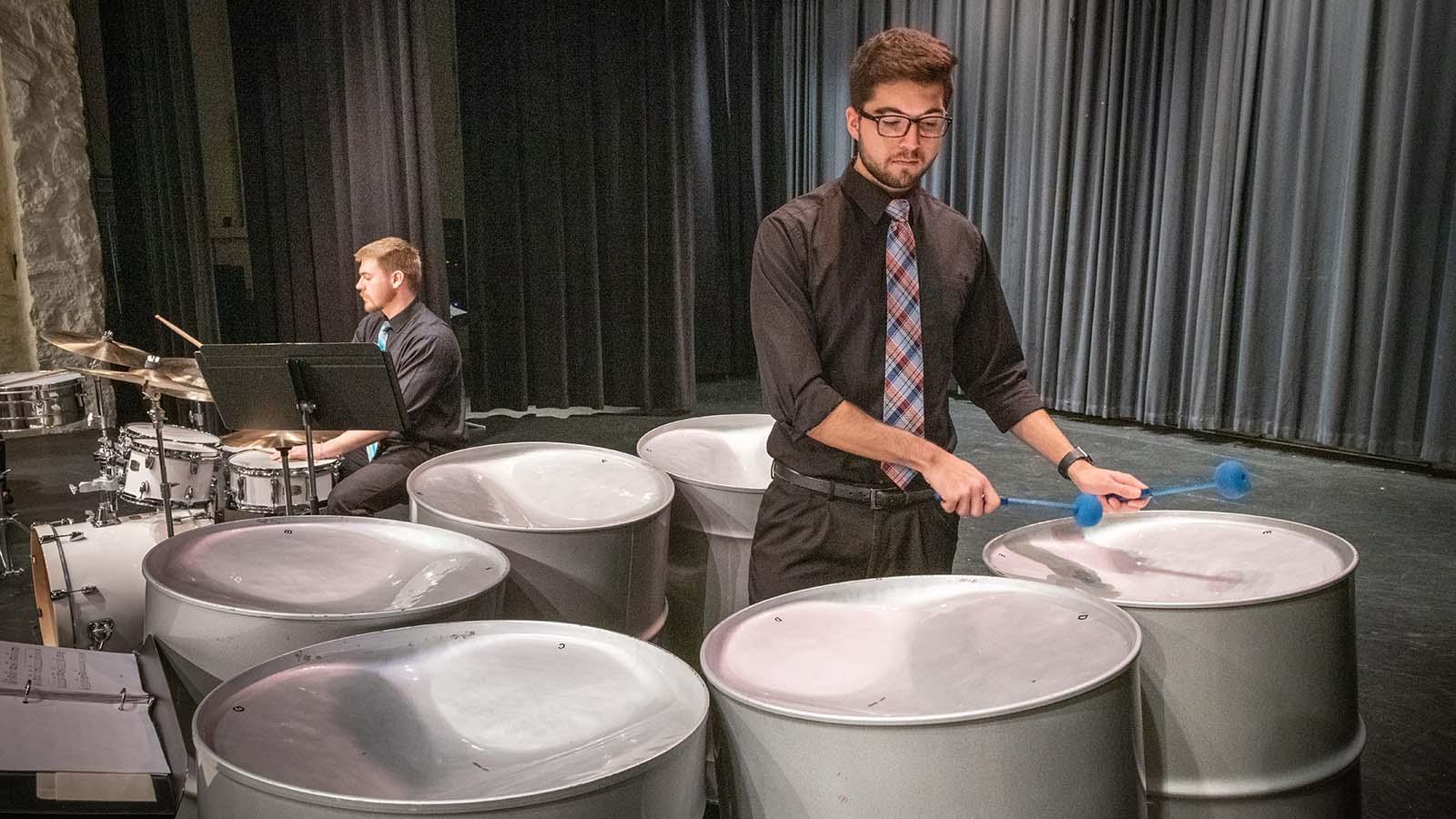 Music student playing steel pans on stage with another student behind him