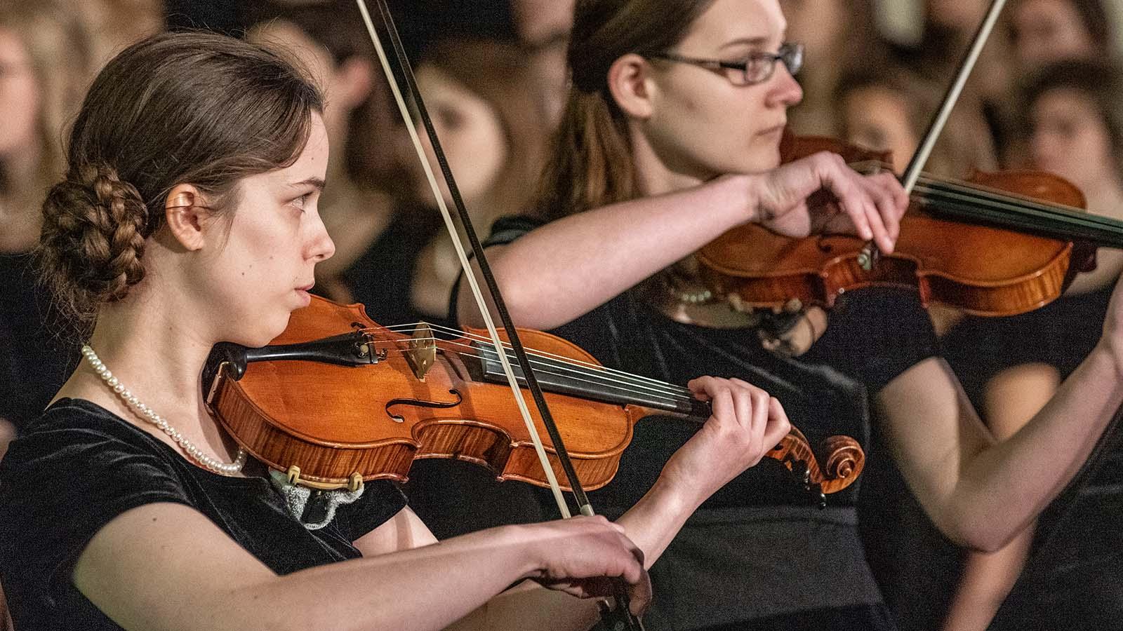 Two members of the string ensemble performing in front of choir