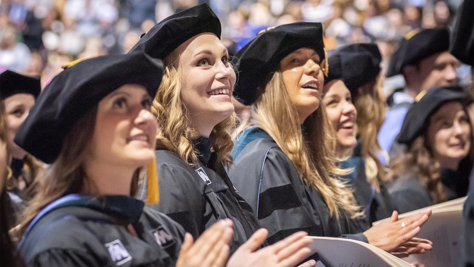 Three female University of Mary students sitting among a crowd of their fellow graduates.