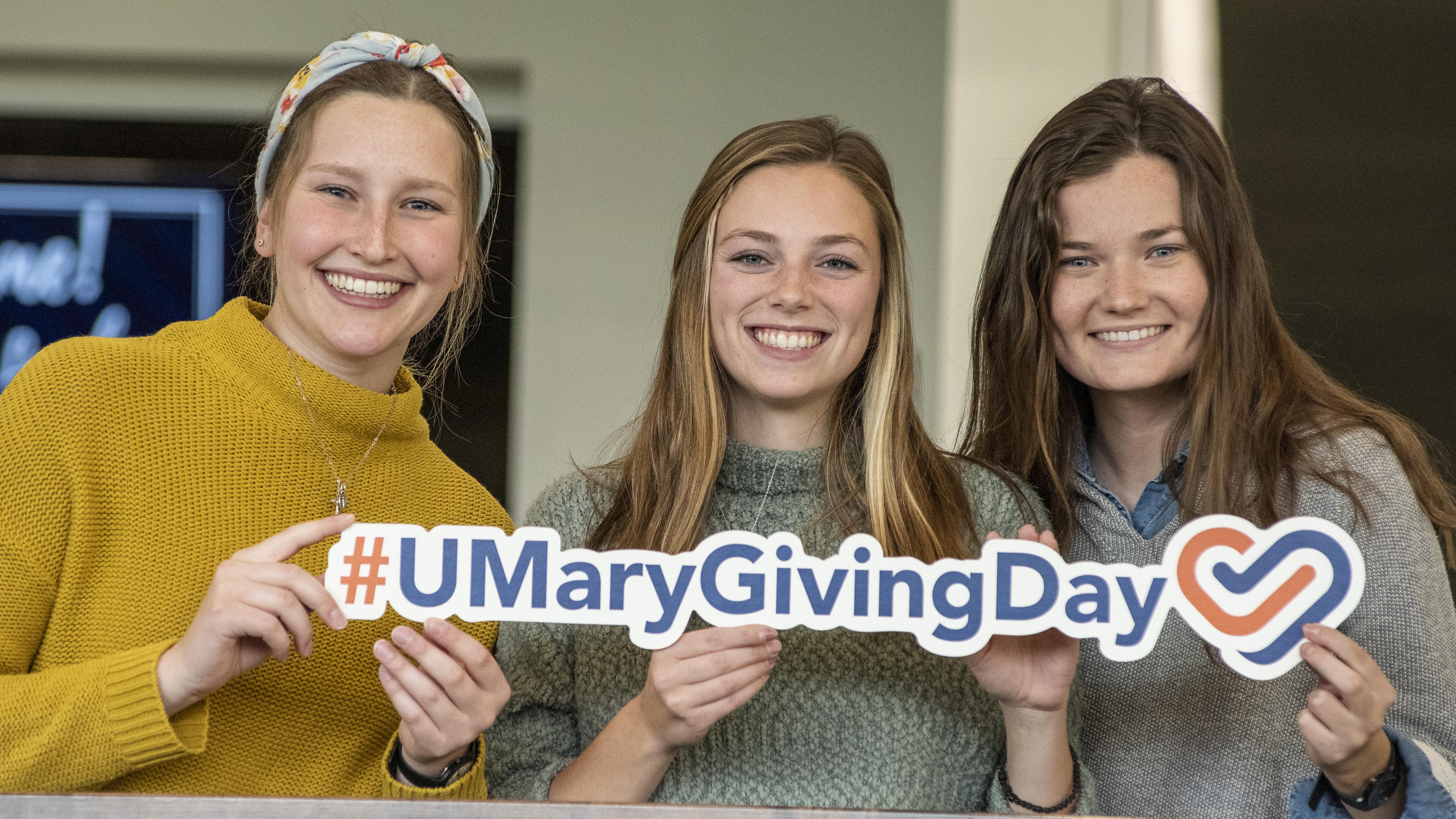 Three female students holding a #UMaryGivingDay sign