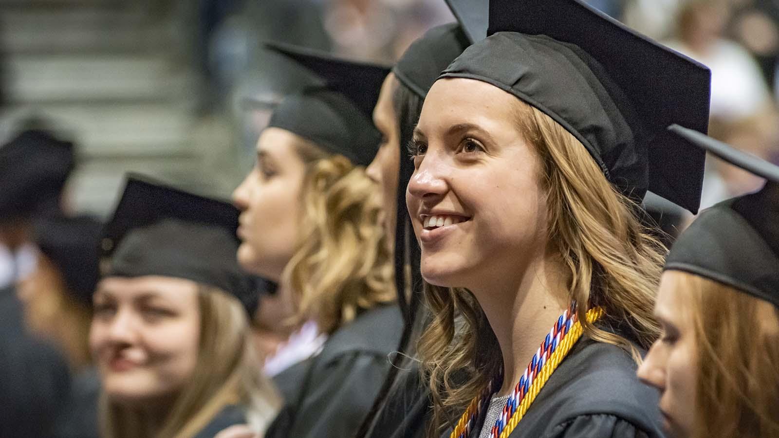 Happy female graduate at commencement with several students in the background.