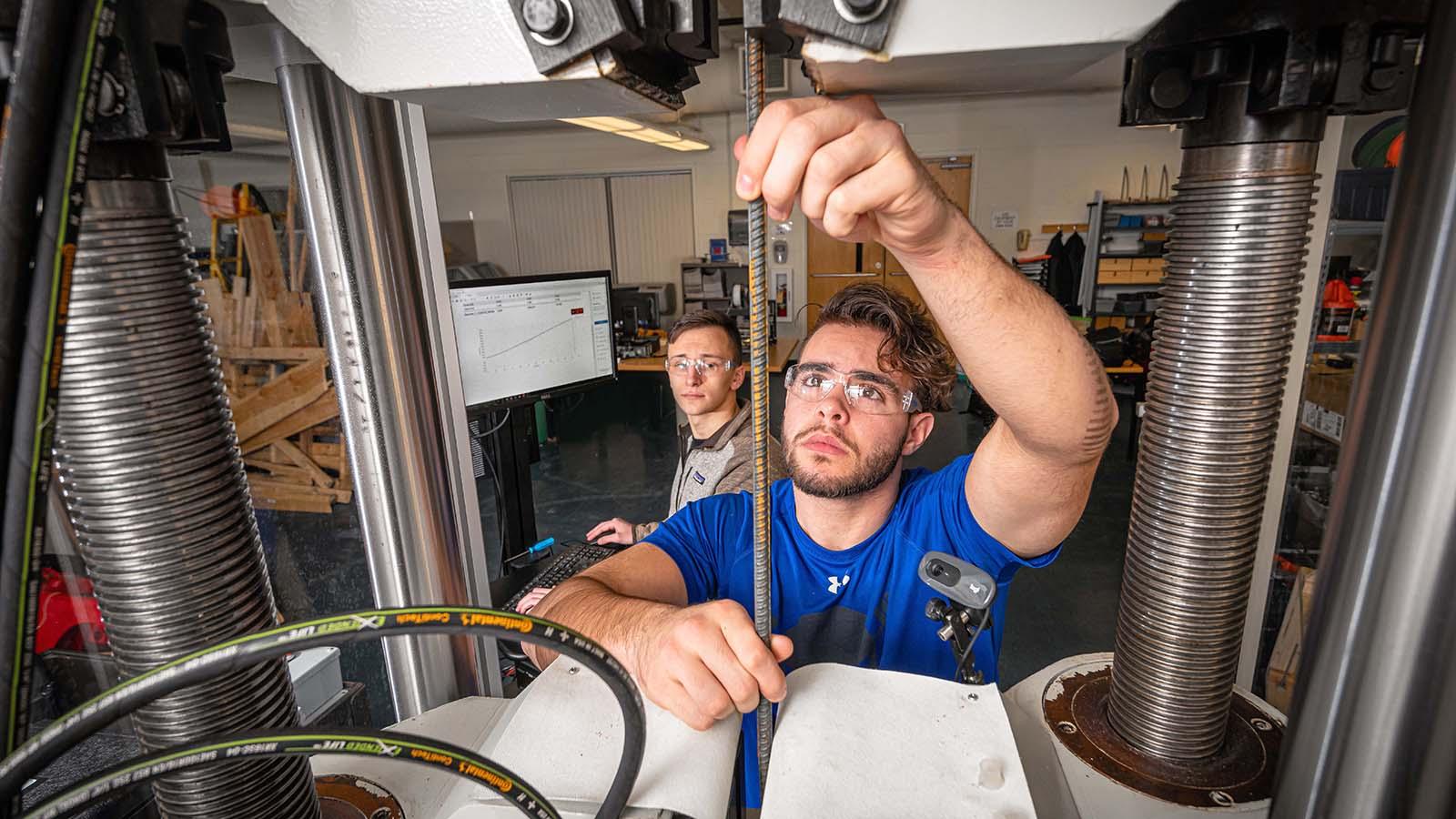 Two construction management students in shop cutting rebar