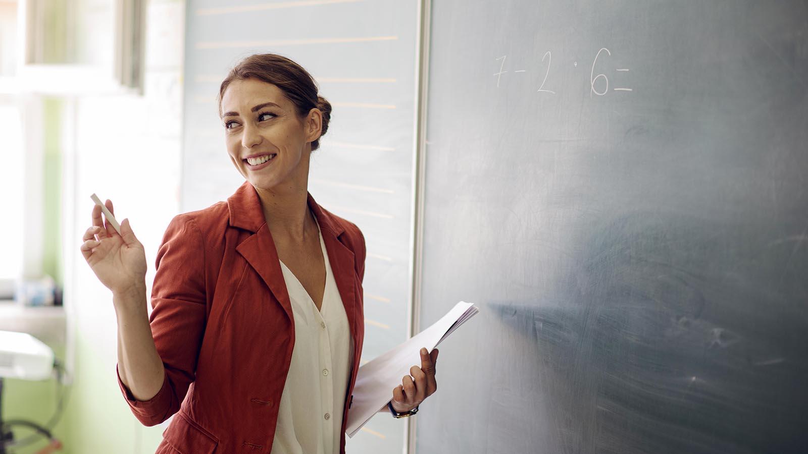 Young female teacher standing in front of the blackboard and demonstrating how to multiply numbers