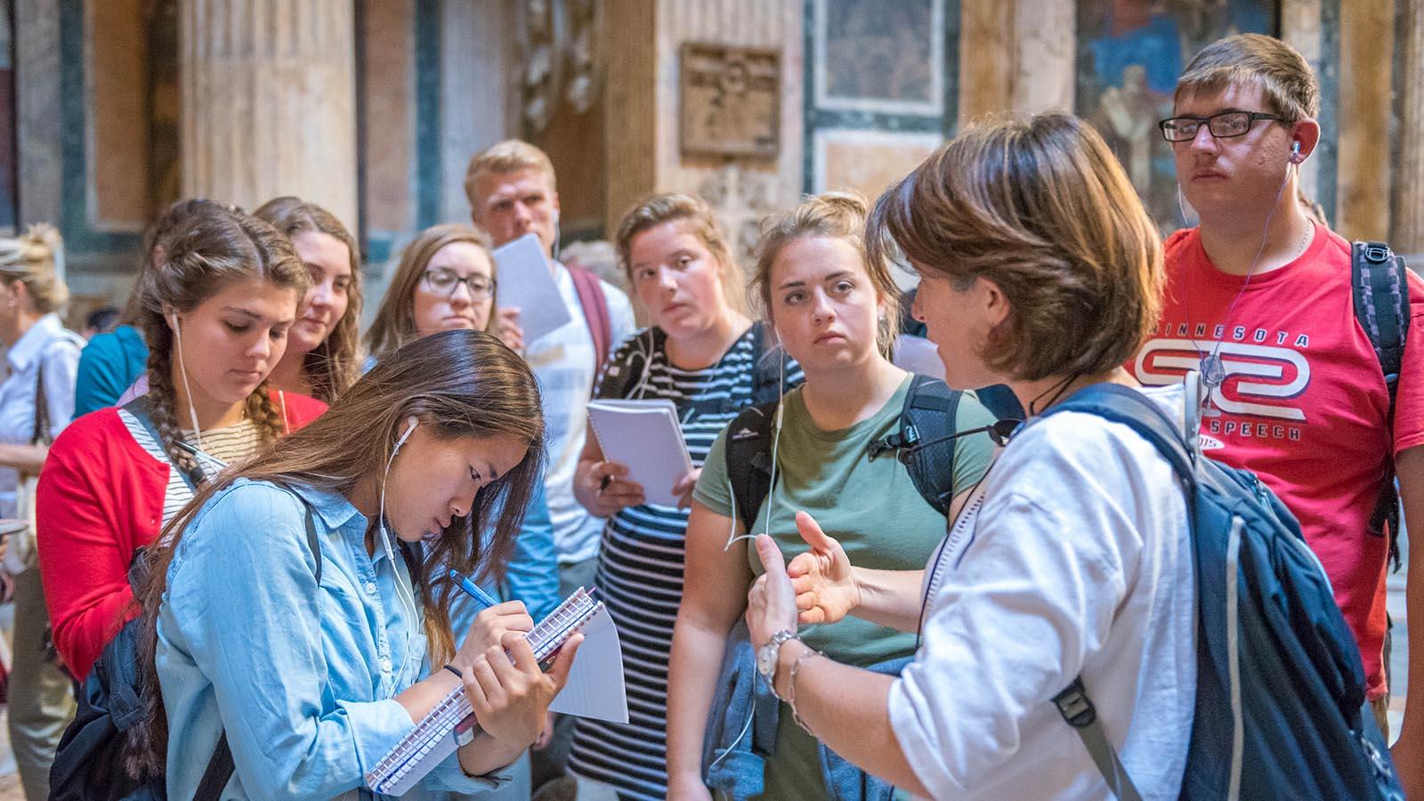 Study abroad students in the Pantheon in Rome, Italy, taking notes while listening to lecture by a professor