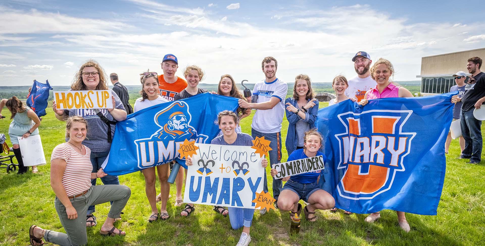 Students smiling holding up welcome signs and UMary flags.