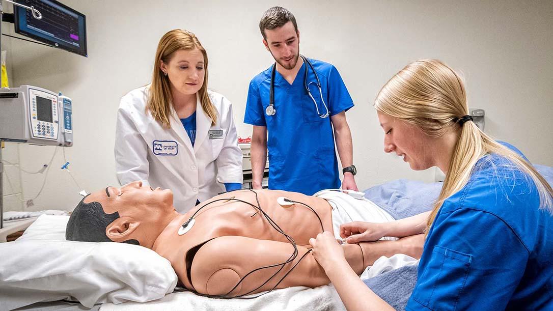Nursing students with faculty in simulation lab inserting an IV in the arm of a mannequin