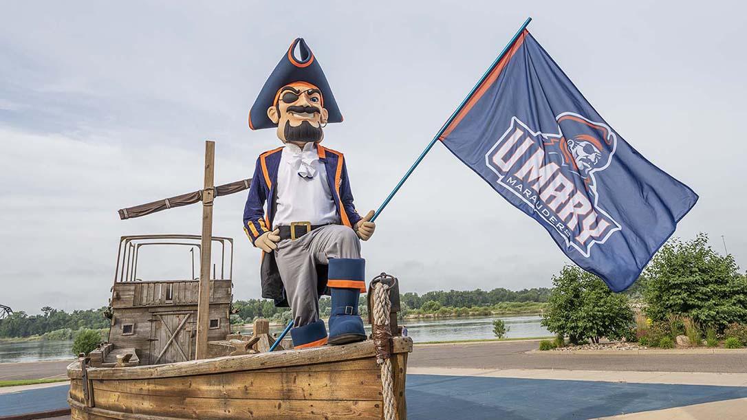 Max the Marauder standing on the front of a boat with a Marauders flag 