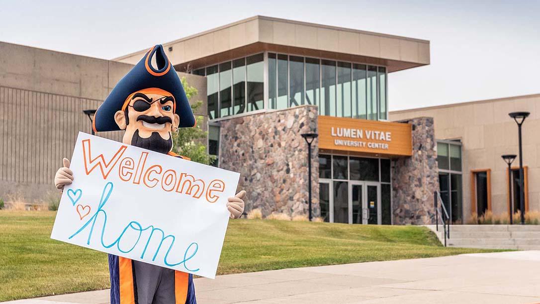 Max the Marauder holding a welcome home sign in front of the university center