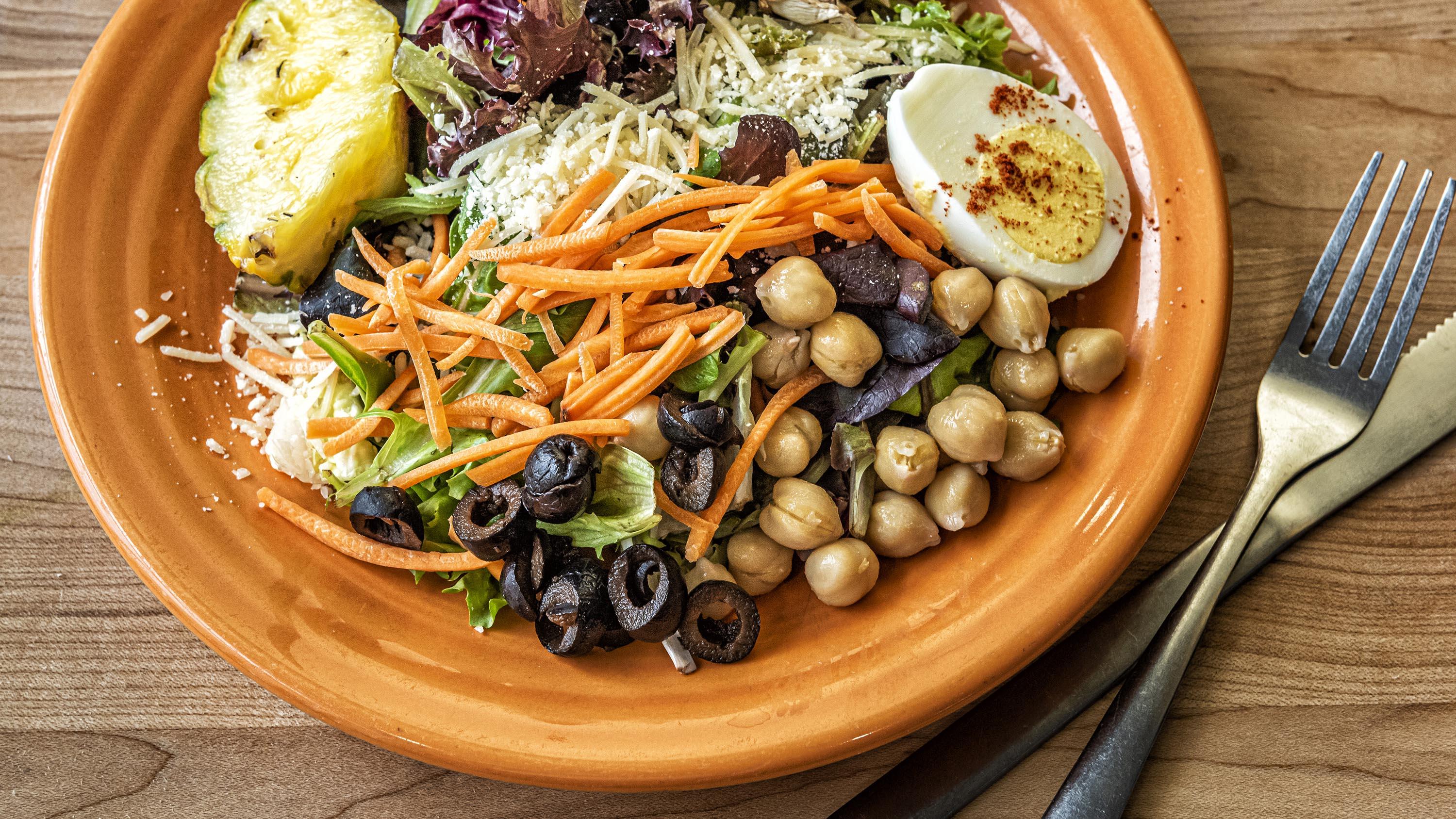 Salad, shredded carrots, black olives, and hard-boiled eggs on an orange plate in the Crow’s Nest Campus Restaurant.