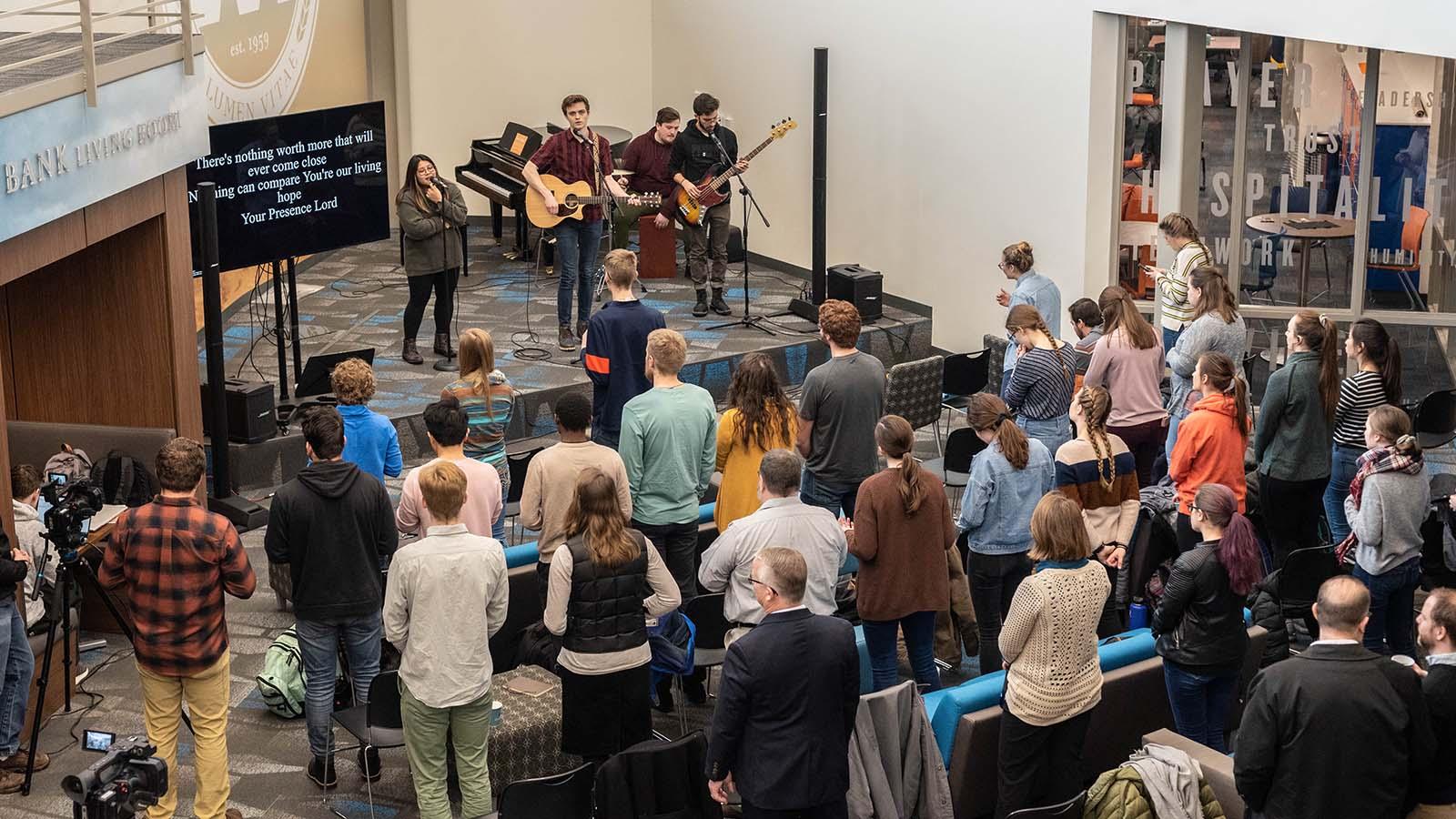 Large group of students gathered for worship with four musicians on stage 