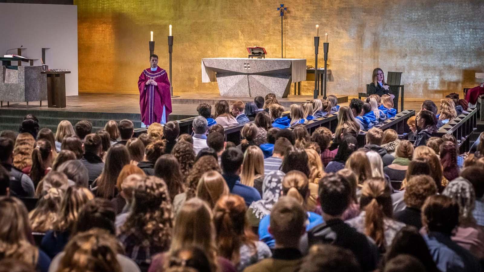 Priest giving a homily to a large number of students