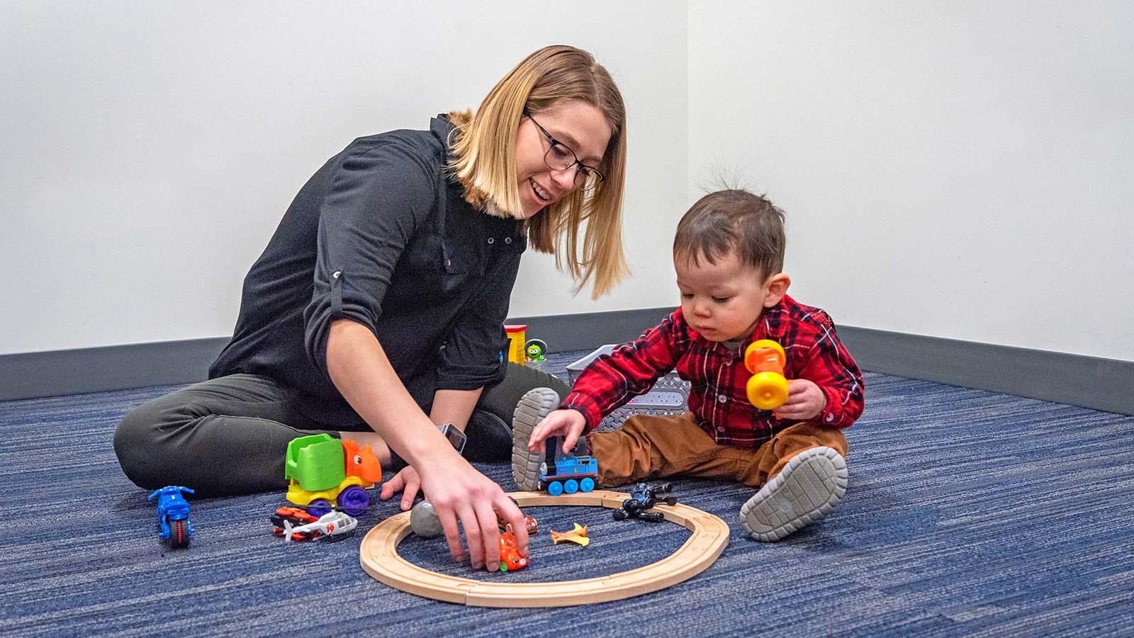 Speech-language pathology student sitting on floor with toddler client and playing with toys