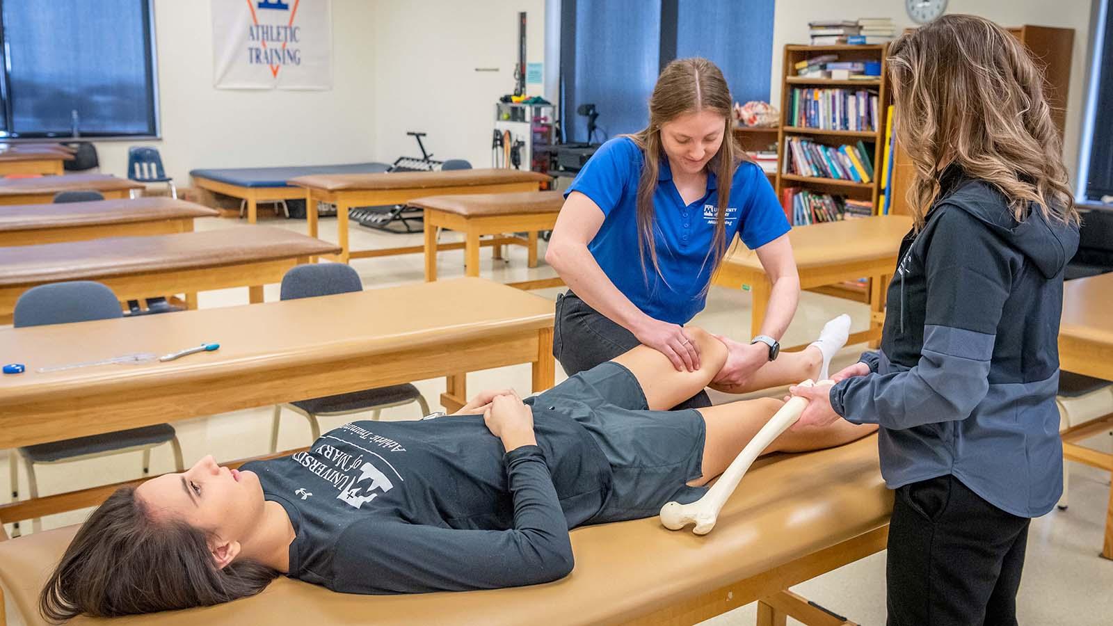 Athletic training student completing an assessment on athlete’s knee while instructor is watching