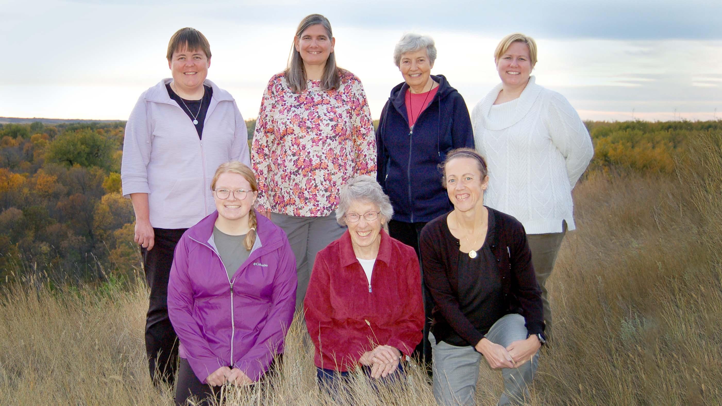Seven Sisters of Annunciation Monastery posing for photo in the tall grass along the bluff outside the monastery with fall colored trees in the background.